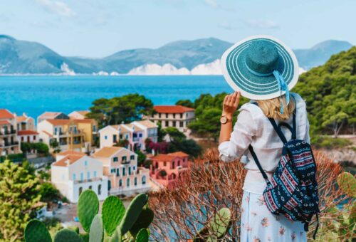 Tourist female with blue sun hat and travel backpack enjoying greek vivid colored Assos town